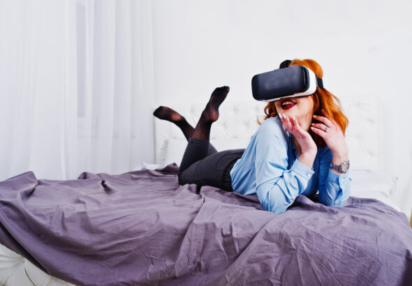 Red haired girl in bed with vr glasses at studio room.